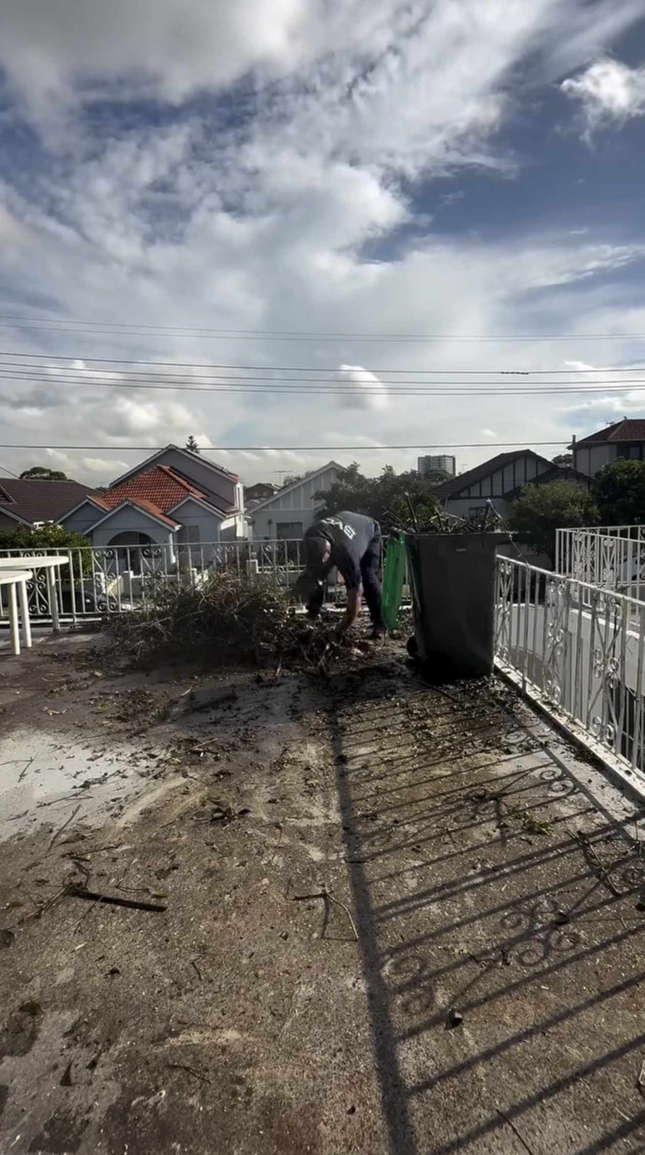 BVC crew member loading cut branches into a green waste bin on a terrace